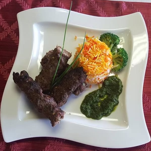 Indian seekh kebabs with orange rice, broccoli, and green chutney on a white plate.