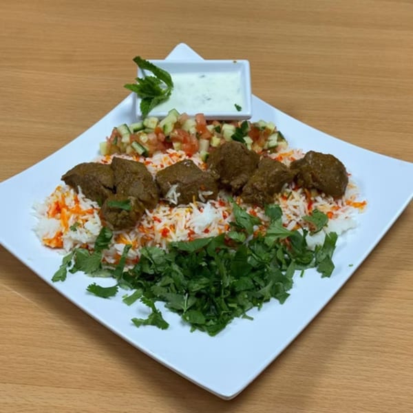 Indian lamb curry with rice, fresh cilantro, a side salad, and raita on a white plate.