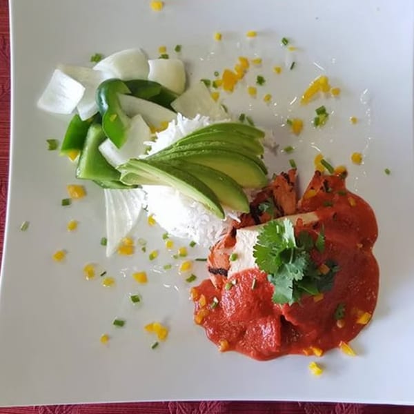 Indian dish with red curry chicken, white rice, sliced avocado, onions, and green peppers.