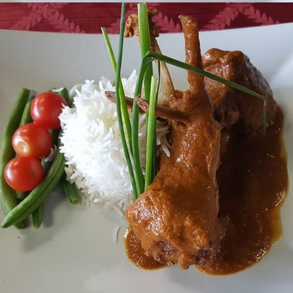 Indian lamb curry with rice, green beans, cherry tomatoes, and chives on a white plate.