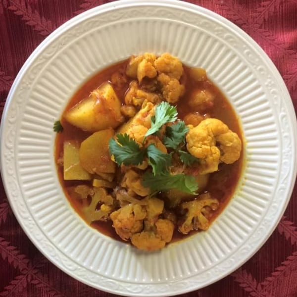 Aloo Gobi, an Indian dish with cauliflower and potatoes in a rich, orange curry sauce, garnished with cilantro.