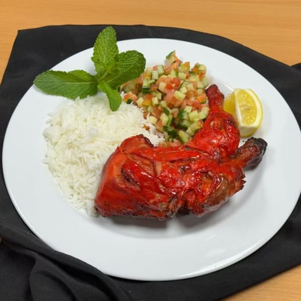Taste of Curry's Tandoori Chicken with rice, mint, cucumber-tomato salad, and a lemon wedge.