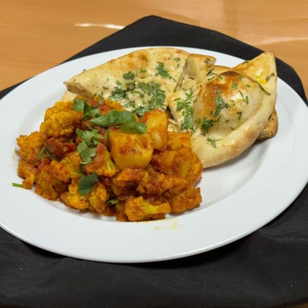 Indian aloo gobi, a potato and cauliflower curry, with naan bread on a white plate.